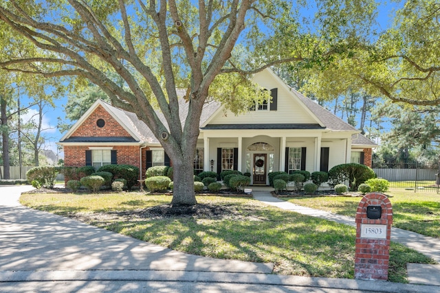 view of front of property with covered porch, brick siding, fence, and a front lawn