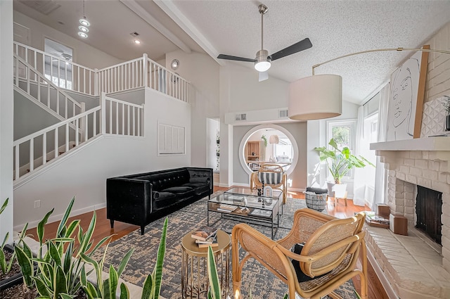 living room featuring stairway, a ceiling fan, a brick fireplace, a textured ceiling, and wood finished floors