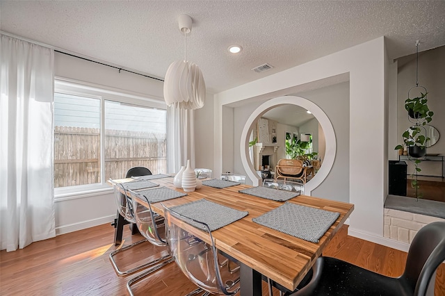 dining area featuring a textured ceiling, a fireplace, wood finished floors, visible vents, and baseboards