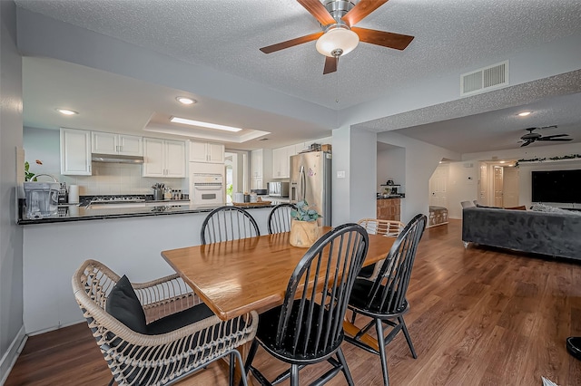 dining room featuring dark wood-style floors, a tray ceiling, visible vents, a ceiling fan, and a textured ceiling