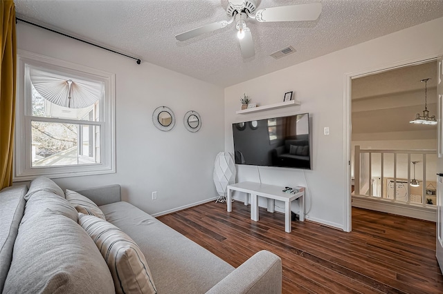 living area with a textured ceiling, wood finished floors, visible vents, baseboards, and a ceiling fan