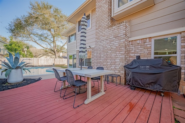 wooden deck with outdoor dining area, fence, grilling area, and a fenced in pool