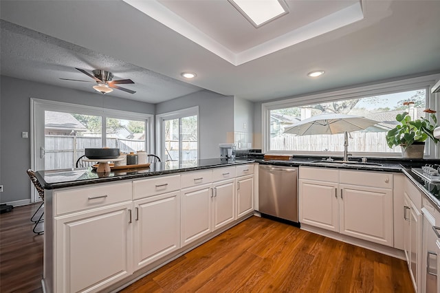 kitchen with a peninsula, a sink, wood finished floors, white cabinets, and stainless steel dishwasher