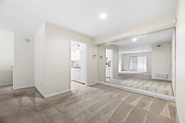 carpeted empty room with visible vents, a sink, and baseboards