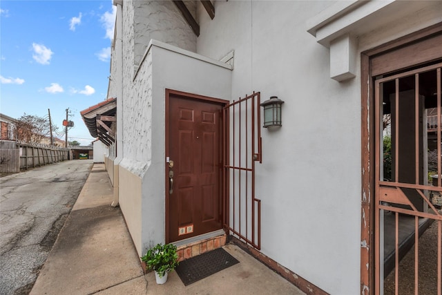 view of exterior entry with fence and stucco siding