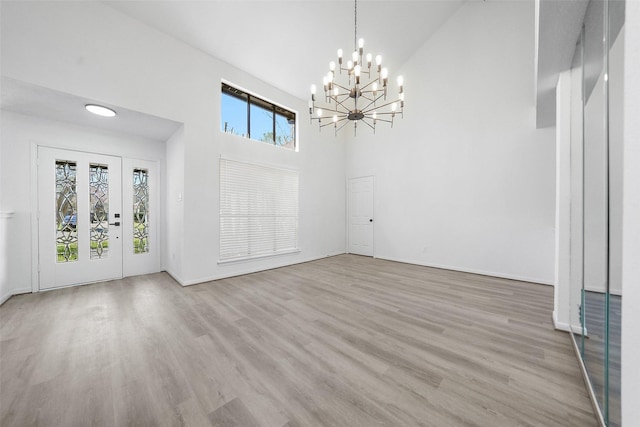 interior space with baseboards, a high ceiling, an inviting chandelier, and wood finished floors