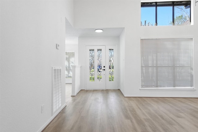 foyer entrance with plenty of natural light, a high ceiling, visible vents, and wood finished floors