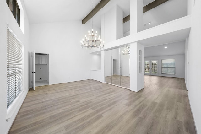 unfurnished living room with beam ceiling, french doors, an inviting chandelier, and wood finished floors