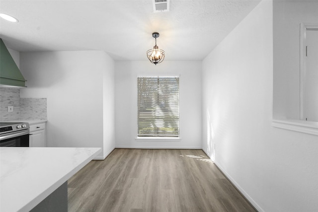 unfurnished dining area with visible vents, an inviting chandelier, baseboards, and light wood-style floors