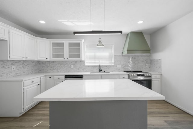 kitchen featuring dark wood-type flooring, wall chimney range hood, appliances with stainless steel finishes, white cabinets, and a sink