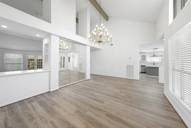 unfurnished living room with visible vents, a chandelier, wood finished floors, high vaulted ceiling, and a sink