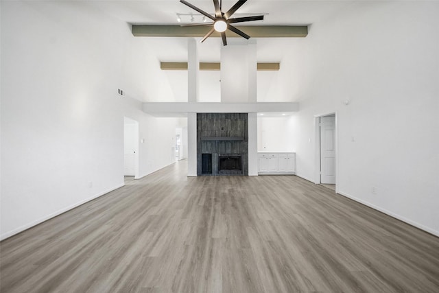 unfurnished living room featuring visible vents, a tiled fireplace, lofted ceiling with beams, wood finished floors, and baseboards