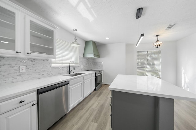 kitchen with light wood-style flooring, a sink, backsplash, stainless steel appliances, and custom exhaust hood