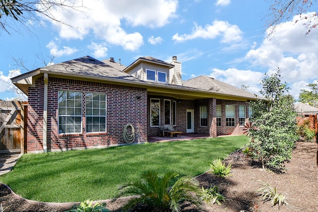 back of house featuring roof with shingles, brick siding, a chimney, a patio area, and a lawn