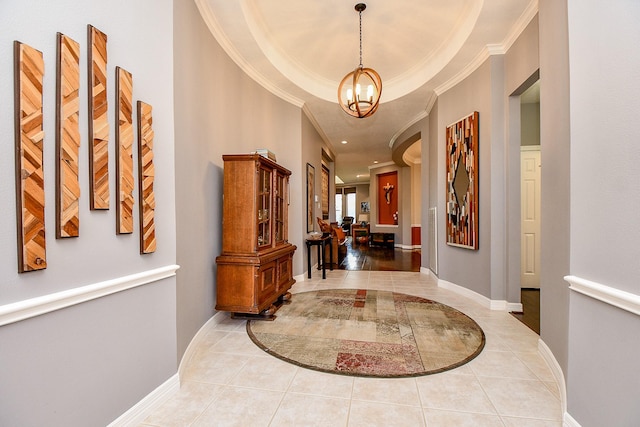 hallway featuring a tray ceiling, crown molding, tile patterned flooring, baseboards, and a chandelier