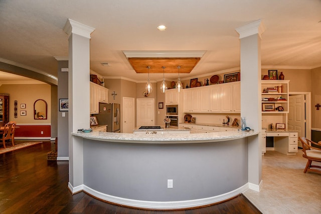 kitchen with a tray ceiling, ornamental molding, a peninsula, stainless steel appliances, and ornate columns