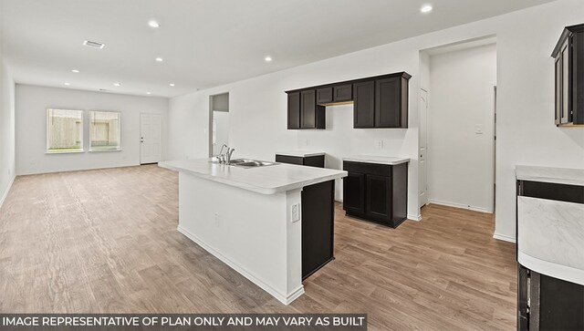 kitchen with light wood finished floors, recessed lighting, light countertops, a kitchen island with sink, and a sink