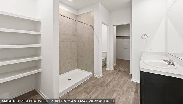 full bathroom with a spacious closet, a stall shower, vanity, wood finished floors, and baseboards