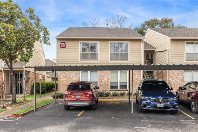 multi unit property with covered parking, brick siding, and roof with shingles