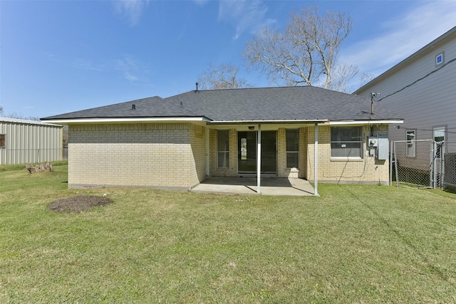 back of property featuring brick siding, fence, roof with shingles, a lawn, and a patio area