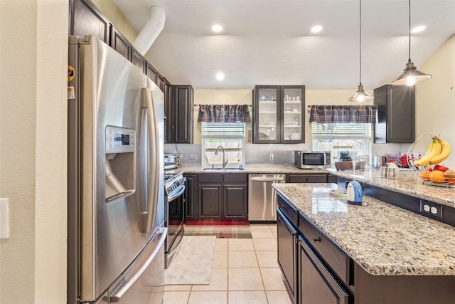 kitchen featuring light tile patterned floors, glass insert cabinets, appliances with stainless steel finishes, light stone counters, and a sink