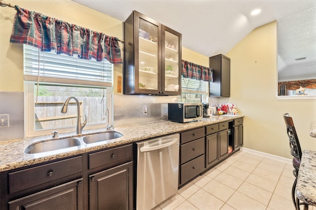 kitchen featuring dark brown cabinetry, light tile patterned floors, glass insert cabinets, stainless steel appliances, and a sink