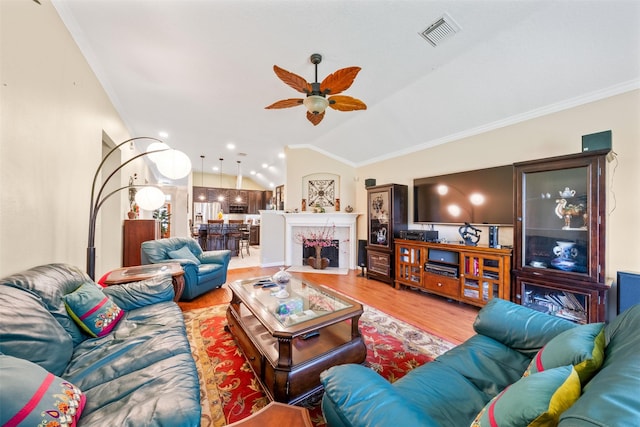 living area with visible vents, lofted ceiling, a fireplace with flush hearth, wood finished floors, and crown molding