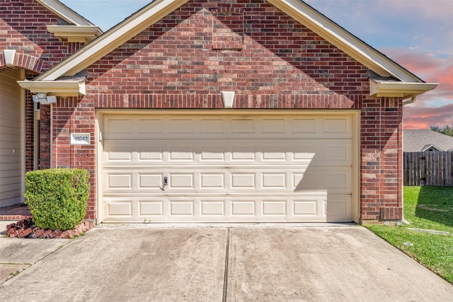 garage at dusk featuring concrete driveway and fence