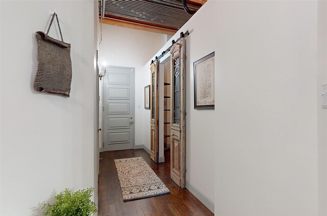 hallway featuring a barn door, wood finished floors, and baseboards