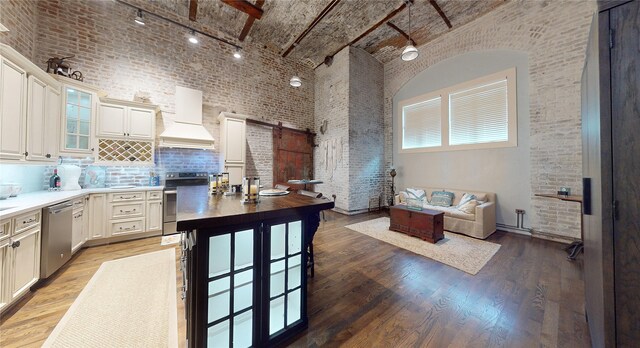 kitchen featuring a barn door, premium range hood, brick ceiling, appliances with stainless steel finishes, and light wood-type flooring