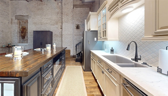 kitchen featuring light wood finished floors, decorative backsplash, butcher block countertops, cream cabinets, and a sink