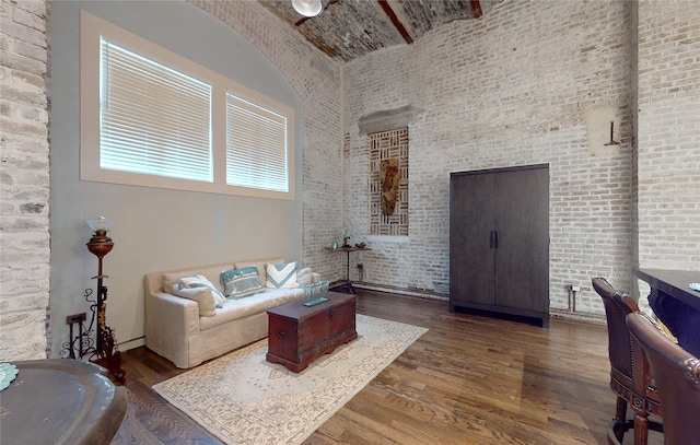 living area with brick wall, a high ceiling, and wood finished floors