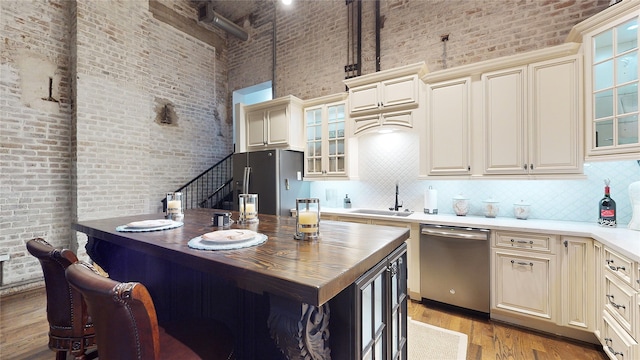 kitchen with a high ceiling, stainless steel appliances, cream cabinetry, light wood-style floors, and a sink