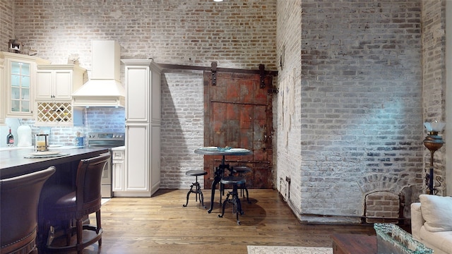 kitchen with a barn door, stainless steel electric range oven, glass insert cabinets, light wood-type flooring, and premium range hood