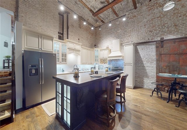 kitchen with stainless steel appliances, brick ceiling, custom range hood, and light wood-style flooring