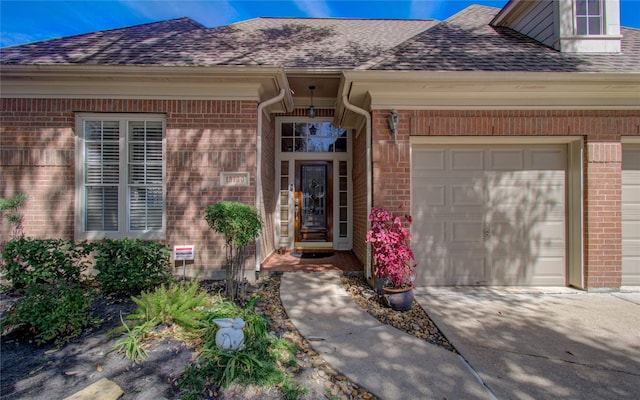 property entrance with a garage, roof with shingles, concrete driveway, and brick siding