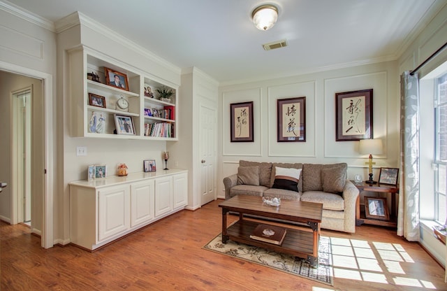 sitting room with ornamental molding, visible vents, a decorative wall, and light wood finished floors