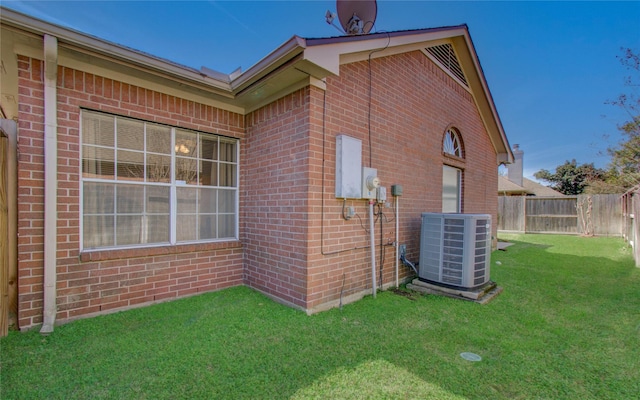 view of side of home featuring brick siding, a yard, fence, and central AC unit