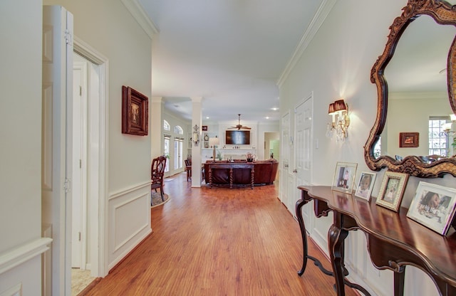 hallway featuring ornate columns, a decorative wall, crown molding, and wood finished floors