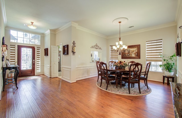 dining area with wood finished floors, visible vents, crown molding, and an inviting chandelier