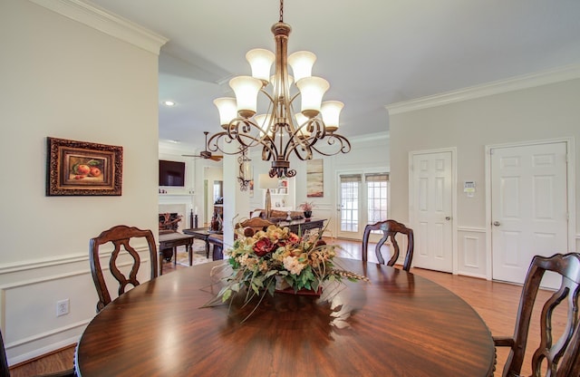 dining space featuring ceiling fan with notable chandelier, a fireplace, wood finished floors, and crown molding