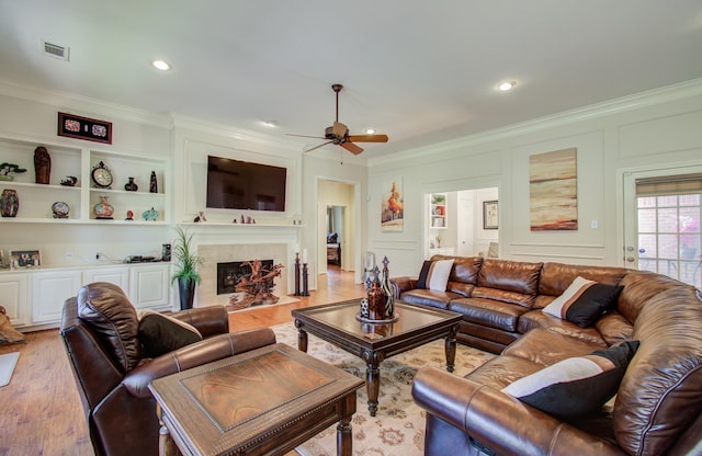 living room featuring a large fireplace, a ceiling fan, light wood-style flooring, crown molding, and a decorative wall