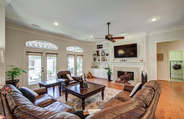 living area with french doors, washer / clothes dryer, visible vents, a tiled fireplace, and light wood-style floors