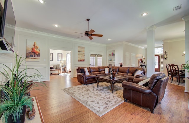 living room featuring visible vents, a ceiling fan, light wood-style flooring, ornamental molding, and a decorative wall