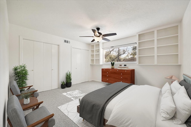 bedroom with visible vents, ceiling fan, a textured ceiling, carpet flooring, and two closets