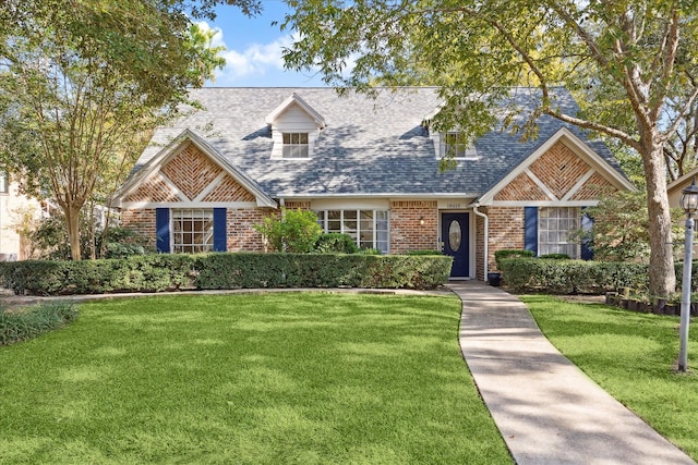 view of front of home with a shingled roof, a front yard, and brick siding