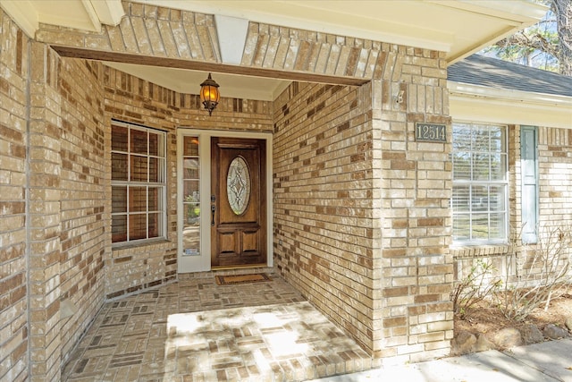 view of exterior entry with covered porch, roof with shingles, and brick siding