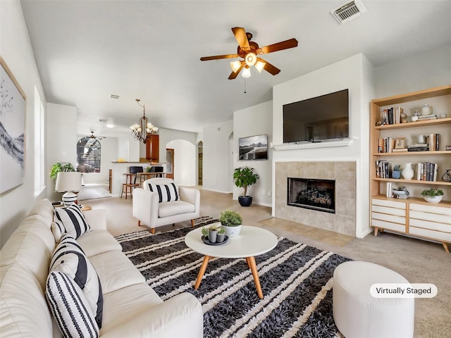 living room featuring visible vents, carpet, a tile fireplace, arched walkways, and a ceiling fan