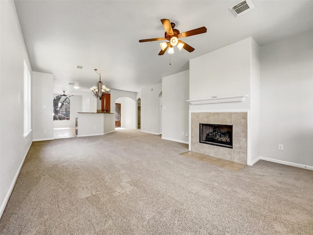 unfurnished living room with visible vents, ceiling fan, carpet floors, a tile fireplace, and arched walkways