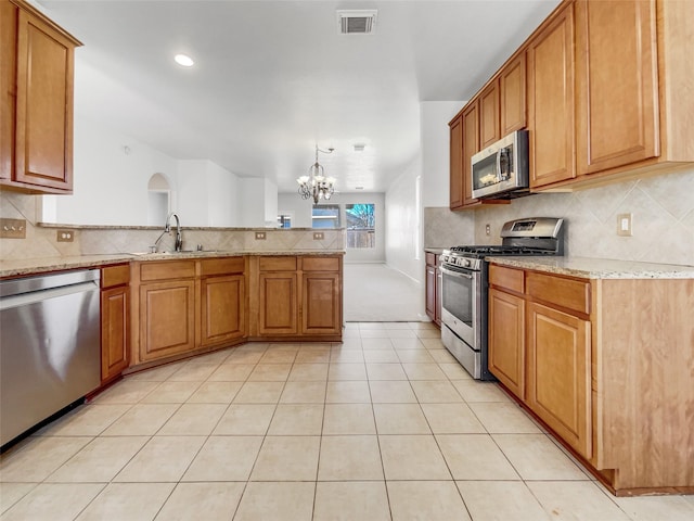 kitchen featuring visible vents, a sink, stainless steel appliances, a peninsula, and light stone countertops